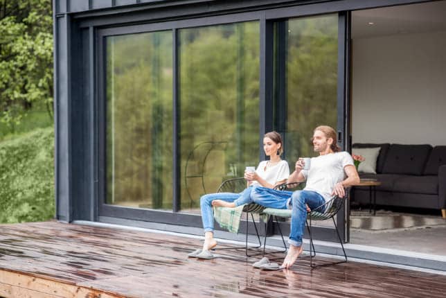 Paar sitzt entspannt auf Terrasse vor großem Fenster